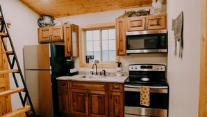 A kitchen with wooden cabinets, stainless steel appliances, a window, and a rooster decoration. - Newly Constructed! "The Stables" (Trenton)