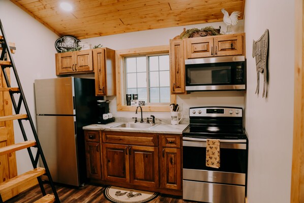 Una cocina con armarios de madera, electrodomésticos de acero inoxidable, una ventana y una decoración con un gallo.