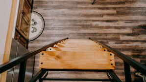 A wooden staircase with metal railings, leading to a room with a wooden floor and a wall-mounted clock. - Newly Constructed! "The Stables" (Trenton)