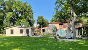 A residential property with a well-maintained lawn, a small house with a red roof, and a larger building with a stone facade.