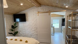 A bedroom with a bed, a TV mounted on the wall, a plant, and a door leading to a bathroom.
