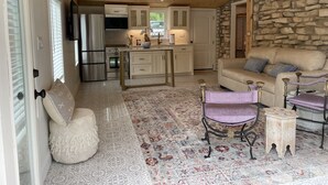 A cozy interior with a stone wall, wooden ceiling, a sofa, a patterned rug, and a kitchen area.