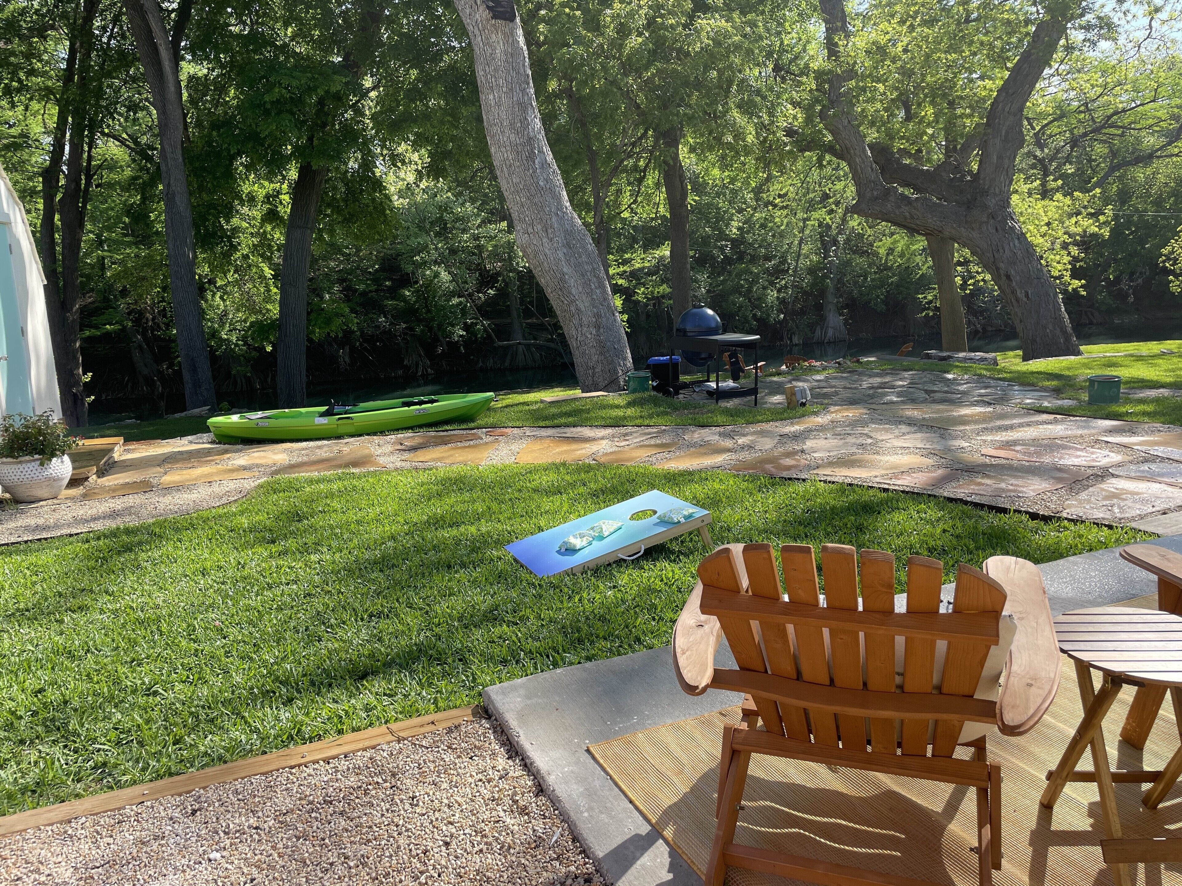 Un jardin avec une pelouse, un banc en bois, une table, un kayak et un barbecue.