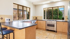 A modern kitchen with a central island, a built-in oven, and large windows offering views of greenery. - Beachside living takes a smart & stylish turn with this well appointed apartment (Lennox Head)