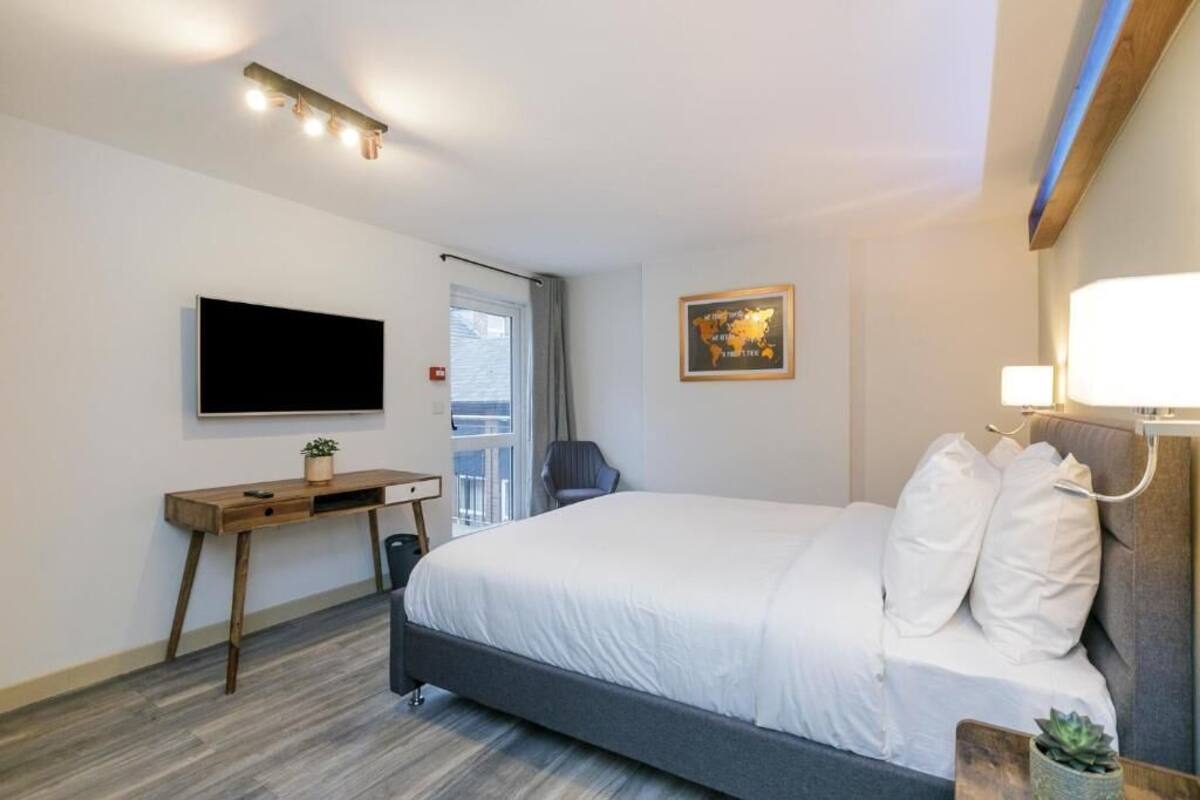 A hotel room with a bed, a desk, a chair, a TV, and a window.