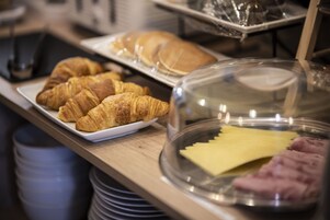 A breakfast buffet with croissants, pancakes, and a cheese and ham display.