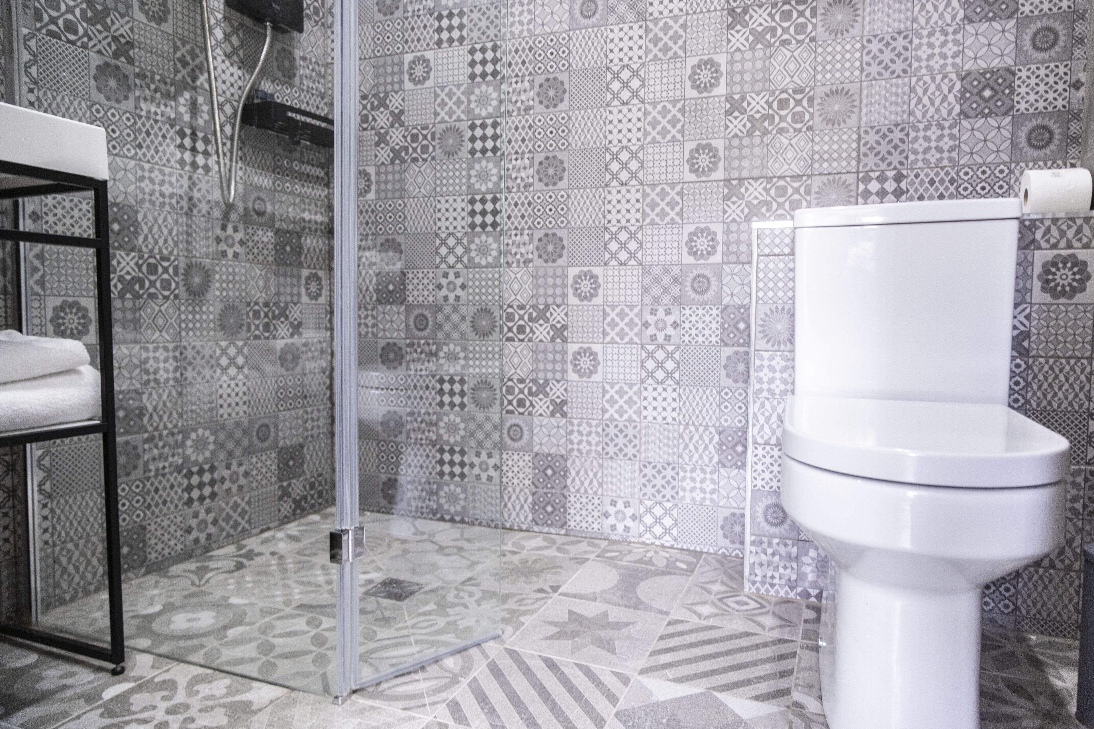 Un baño con baldosas estampadas, un inodoro blanco y una repisa metálica con una toalla.