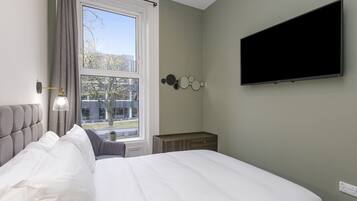 A bedroom with a large bed, a window with curtains, a bedside table, a wall-mounted TV, and a wall decoration.