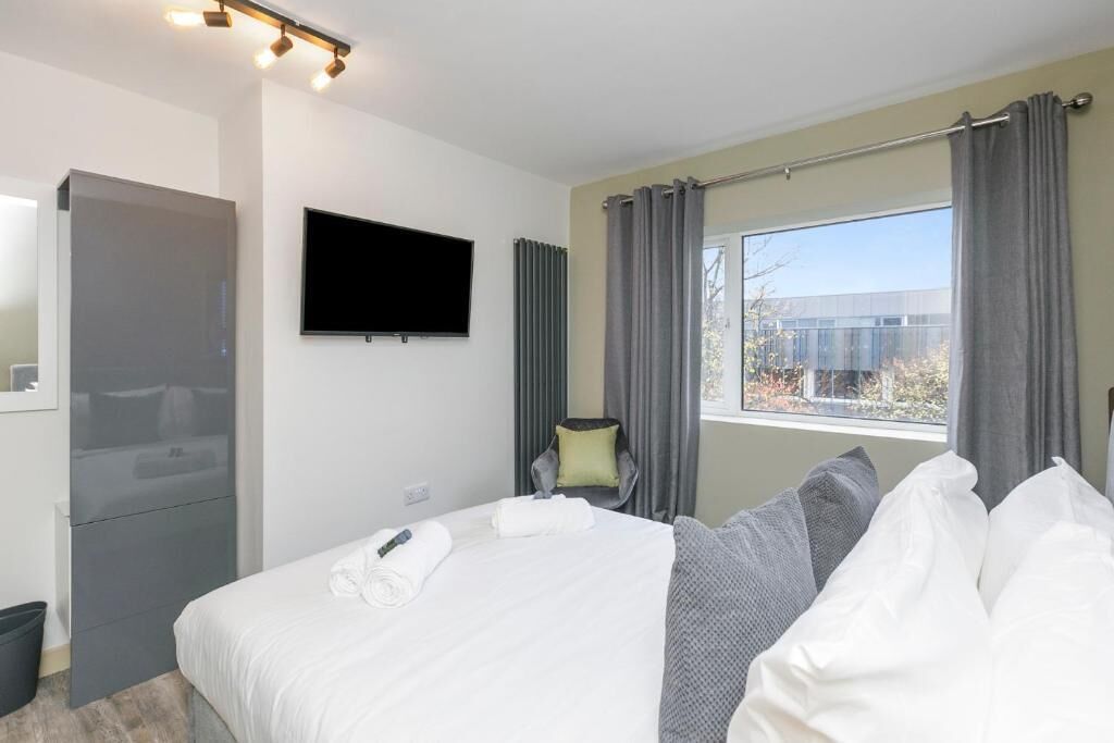 A hotel room with a bed, a flat-screen TV, a window with curtains, and a view of the outside.