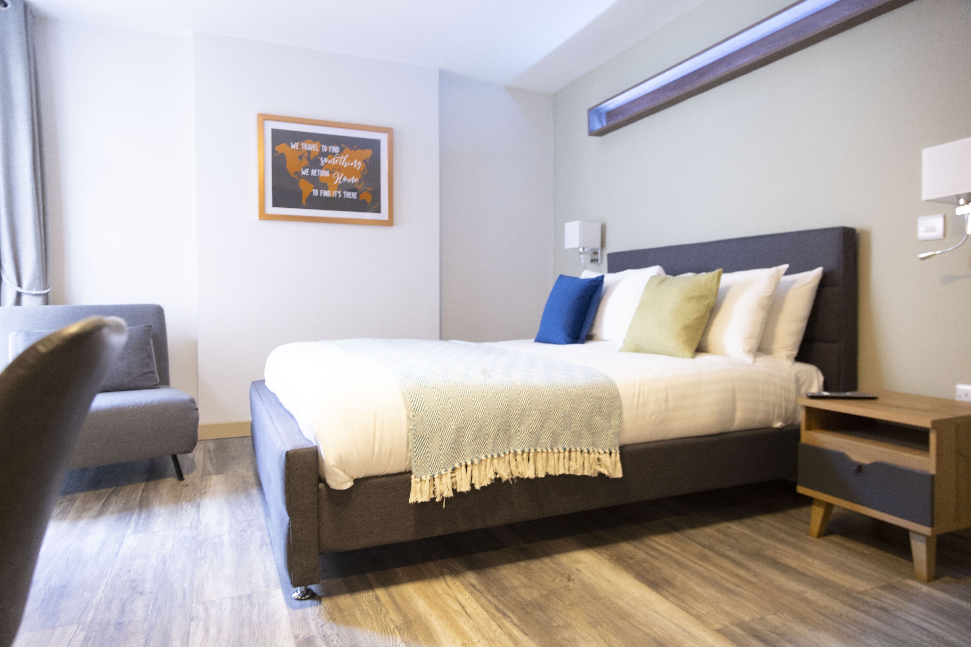 Un dormitorio moderno con una cama grande, una mesita de noche, una silla y una lámpara fijada a la pared.