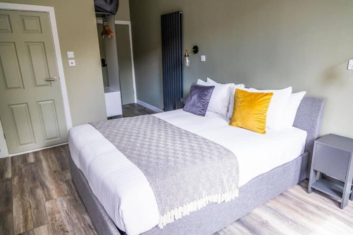 A neatly made bed with a patterned throw, a bedside table, and a door to the left.
