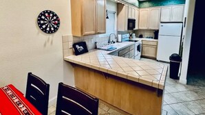 A kitchen with wooden cabinets, a tiled backsplash, and a dartboard on the wall.