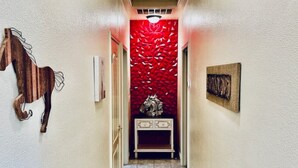A hallway with a red textured wall, a wooden horse decoration, a console table, and a framed picture.