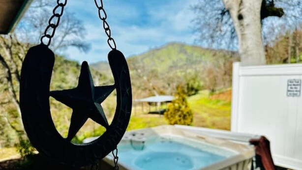 A hot tub with a horseshoe-shaped star decoration hanging above it, set against a backdrop of hills and a white fence.