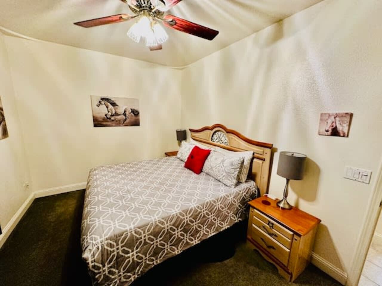 Un dormitorio con cama, mesita de noche, ventilador de techo e imágenes colgadas en la pared.