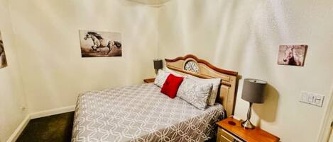 Un dormitorio con cama, mesita de noche, ventilador de techo e imágenes colgadas en la pared.