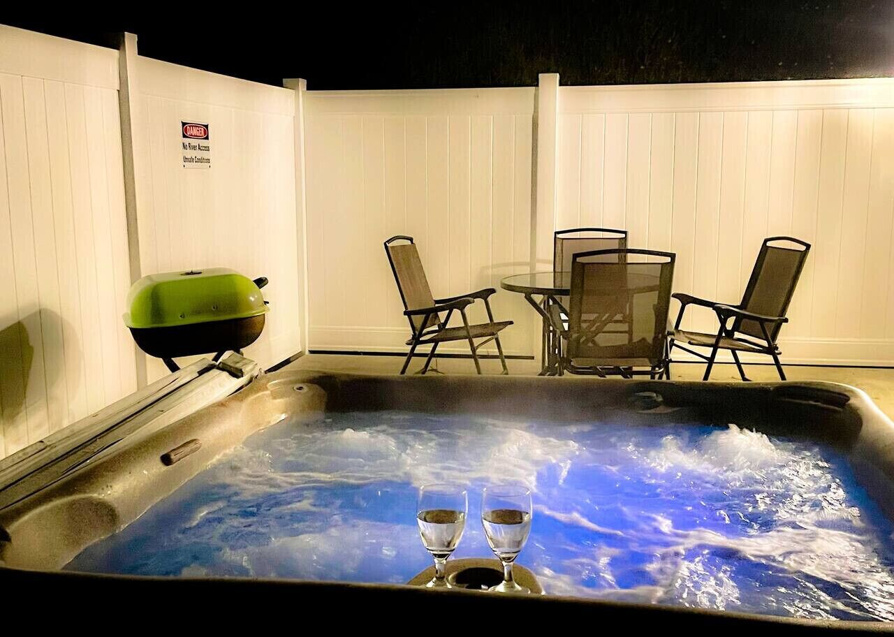 Een hottub met twee glazen, omringd door stoelen en een tafel, voor een witte hek met een 'DANGER' bord.