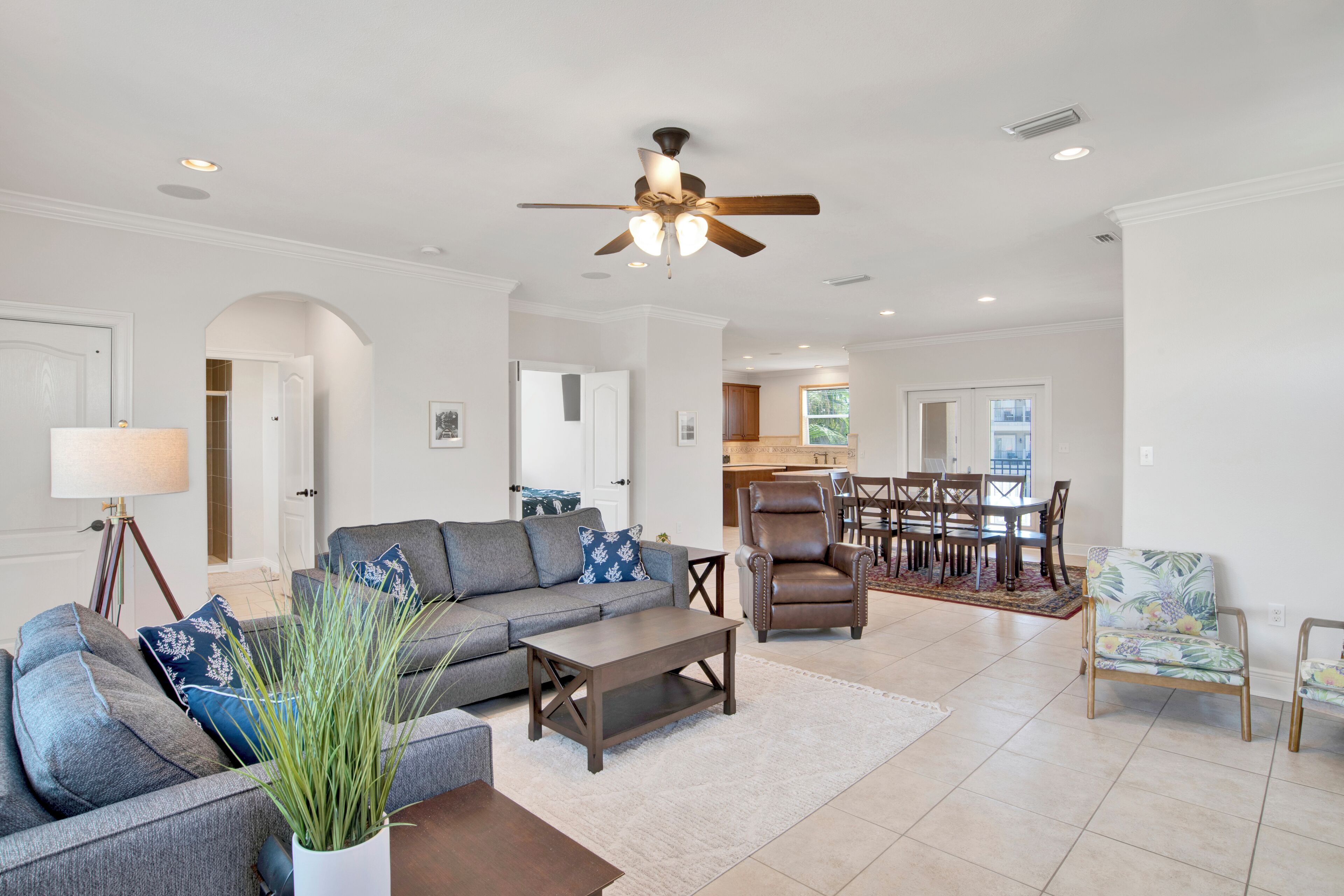 A spacious living room with a gray sectional sofa, a wooden coffee table, and a ceiling fan. There is a dining area with a wooden table and chairs.