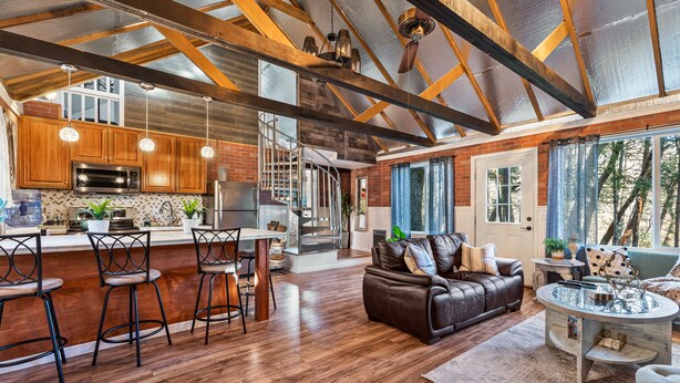 Een ruime woonkamer met houten vloer, een leren bank en een eethoek met barstoelen.