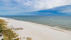 Ein Strand mit einem hölzernen Steg, der zum Wasser führt, einem sandigen Ufer und einem klaren Himmel.