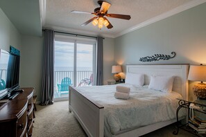 Une chambre à coucher comprenant un lit, un ventilateur de plafond, un bureau avec une lampe, une chaise et une vue sur l’extérieur.