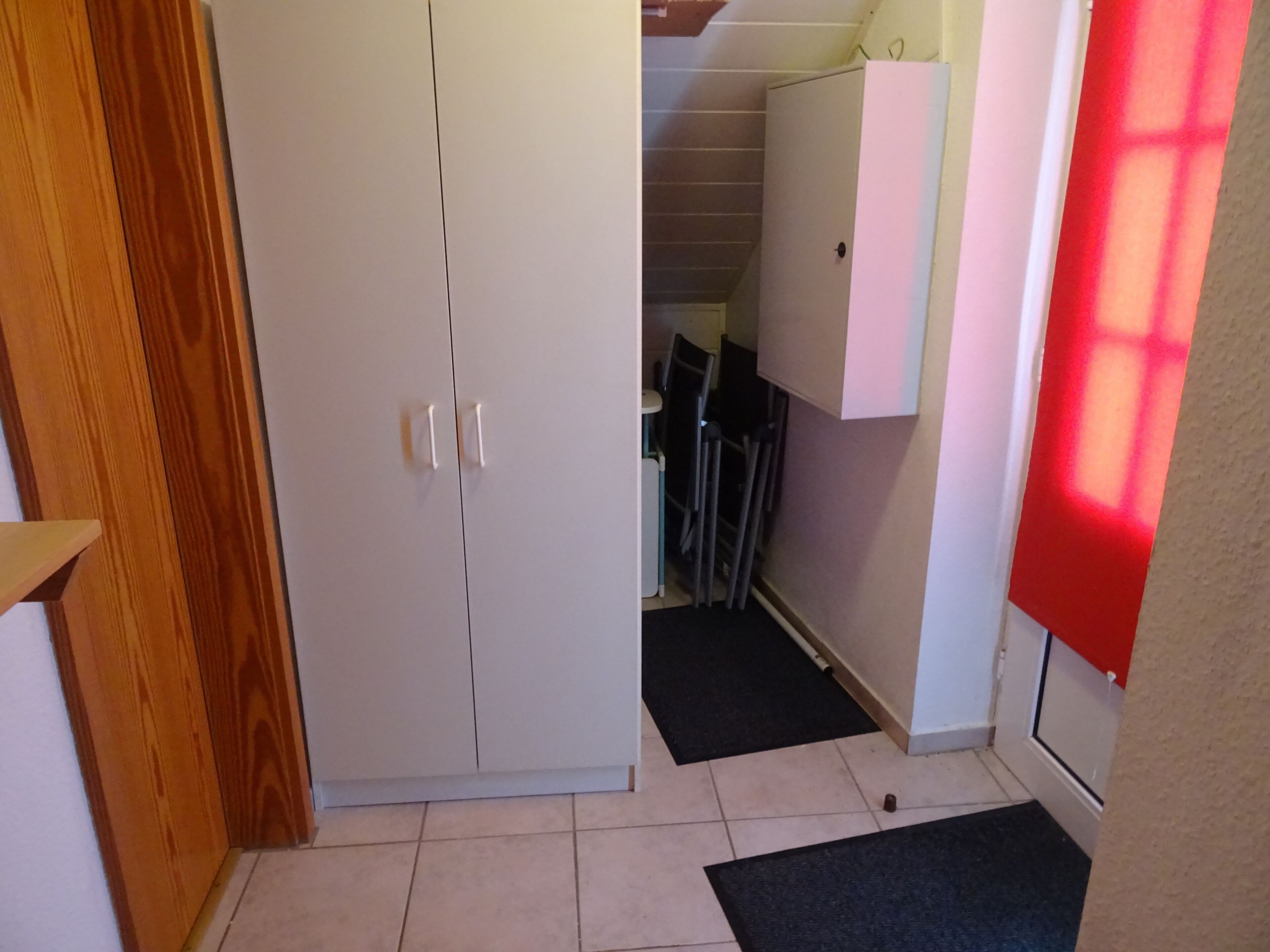 Un couloir avec une porte en bois, une armoire blanche, un tapis noir et un mur rouge.