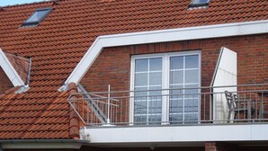 Een gebouw met twee verdiepingen, een dak met rode tegels, een balkon met een metalen hekwerk en een schoorsteen.