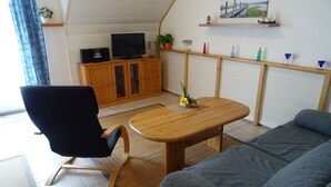Een woonkamer met een houten tafel, een blauwe stoel, een grijze bank, een televisie en een kast met decoratieve objecten.
