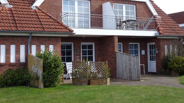 Een tweelaags bakstenen huis met balkon, een kleine tuin en een houten hek.