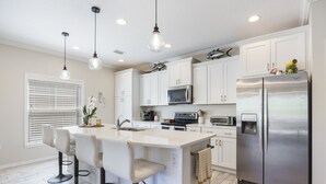 A kitchen with white cabinets, a stainless steel refrigerator, a microwave, and a bar stool island.