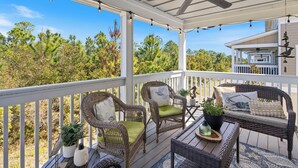 A covered porch with wicker furniture, potted plants, and a view of surrounding trees.