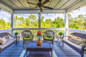 Relax on the covered deck with comfortable wicker sofas and chairs, surrounded by lush greenery.