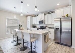 Una cocina con armarios blancos, un refrigerador de acero inoxidable, un microondas y una isla con taburete.