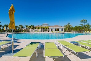 Une piscine avec des chaises longues et un parasol jaune, entourée de palmiers et d’un bâtiment en arrière-plan.