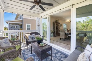 Un espace extérieur abrité, aménagé avec des meubles en osier, un ventilateur de plafond et offrant une vue sur l’intérieur de la maison.