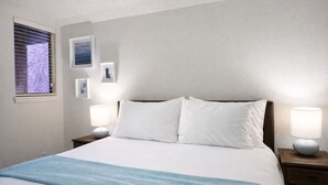 Un llit ben fet amb llençols blancs i una manta blava, flanquejat per dues taules de nit amb làmpades, en una habitació amb un disseny senzill i net.
