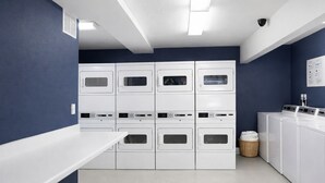 A laundry room with multiple white washing machines and dryers, a white counter, and a blue wall. - Down Town Convenience, TRAX, Self Check-In Studio (Salt Lake City)