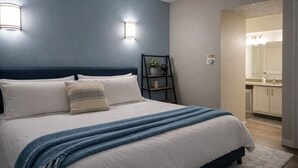 A neatly made bed with a blue blanket, two wall-mounted lights, a small plant on a shelf, and a bathroom visible through an open door. - King Bed*Extensive Cleaning Protocol*Self Check-In (Salt Lake City)