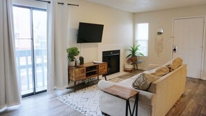 Una sala de estar con sofá, mesa de centro, televisor montado en la pared, chimenea y puerta corrediza de vidrio.