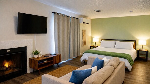 Habitación de hotel con chimenea, una cama con manta verde, un televisor montado en la pared y una mesita de noche con lámpara.