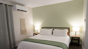 Habitación de hotel con cama, dos lámparas de noche, aire acondicionado en la pared y un colgador de macramé.