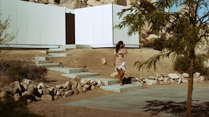 A woman walking on a concrete path beside a modern building with a large open doorway.