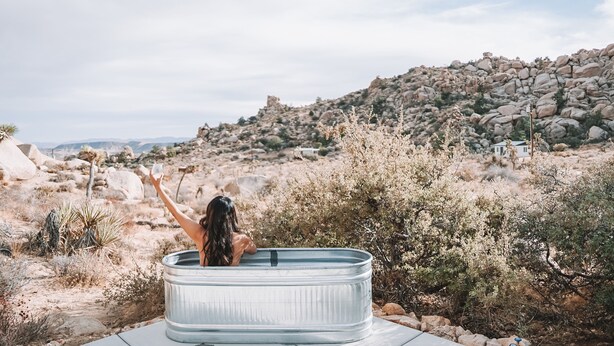 A person relaxing in a hot tub outdoors with a rocky landscape in the background.