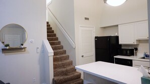 A compact kitchen with a refrigerator, microwave, and a small countertop. A staircase leads to a door with a white frame. - Two Bedroom Loft, King Beds, Down Town Convenience (Salt Lake City)