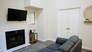 A living room with a fireplace, a grey sofa, a television, and a white door. - Two Bedroom Loft, King Beds, Down Town Convenience (Salt Lake City)