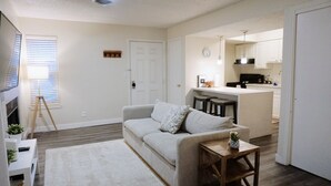 A living room with a sofa, a small wooden table, and a floor lamp. There is a kitchen area with a bar and stools. - Down Town, Award Winning KING Bed, Self Check-In (Salt Lake City)