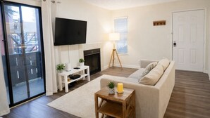 A living room with a sofa, a TV, a fireplace, and a door. - Down Town, Award Winning KING Bed, Self Check-In (Salt Lake City)