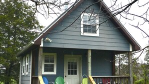 A two-story house with a front porch, a small deck, and a covered area with chairs. - Micro house cabin located near Silver Mines Recreation Area. (Fredericktown)