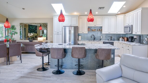 Une cuisine moderne avec des meubles blancs, un îlot central doté de tabourets et des luminaires suspendus.