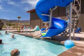 A swimming pool with a blue water slide, surrounded by lounge chairs and a building with a metal exterior.